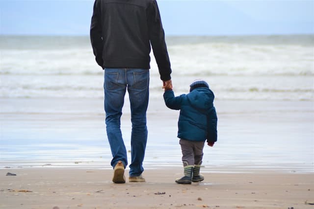 Padre caminando de la mano por la playa con su hijo