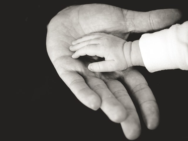Foto en blanco y negro de una mano de padre y la de su hijo.